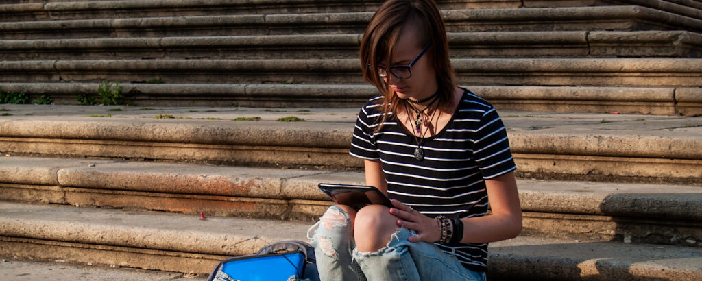 A teenage woman with a tablet on the stairs of a university in a university campus