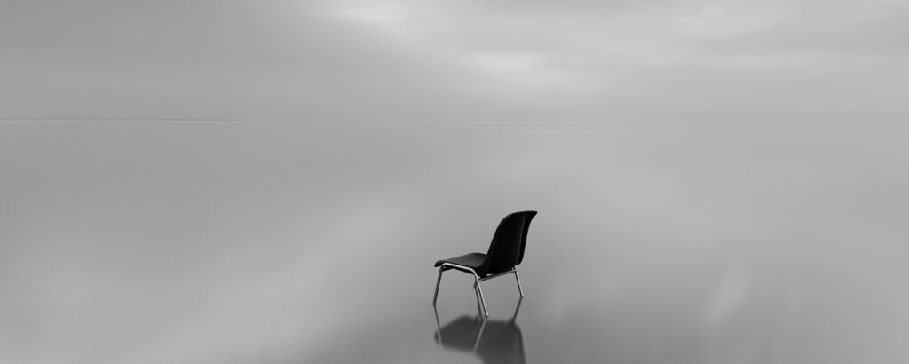 Greyscale shot of a chair on a water surface with a reflection on a rainy day